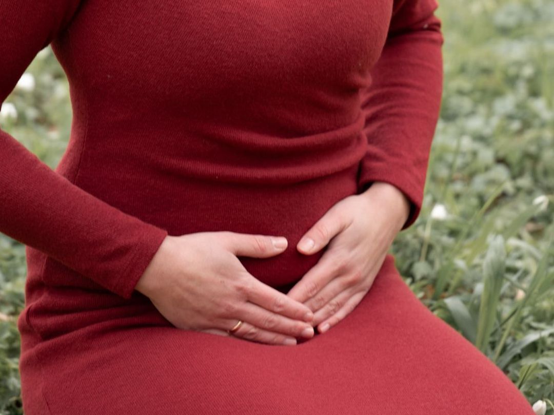 Eine Frau in einem roten Kleid hält ihre Hände auf ihrem Bauch