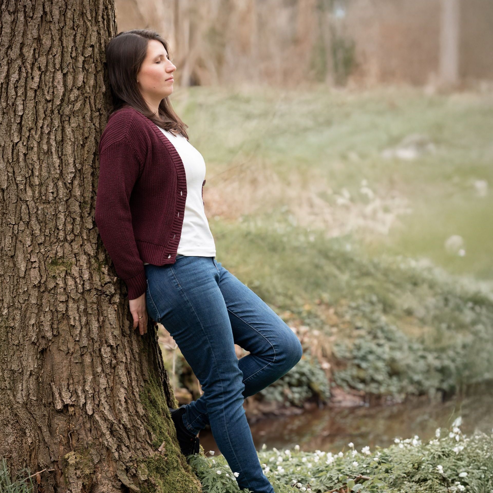 Marie in einem gelben Pullover lehnt an einem Holzpfosten auf einer Brücke.