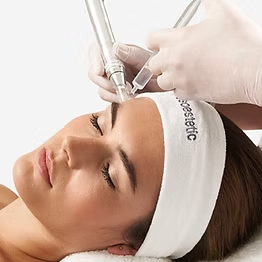 Une personne portant un bandeau blanc reçoit un soin esthétique du visage à l'aide d'un appareil portatif placé sur son front.