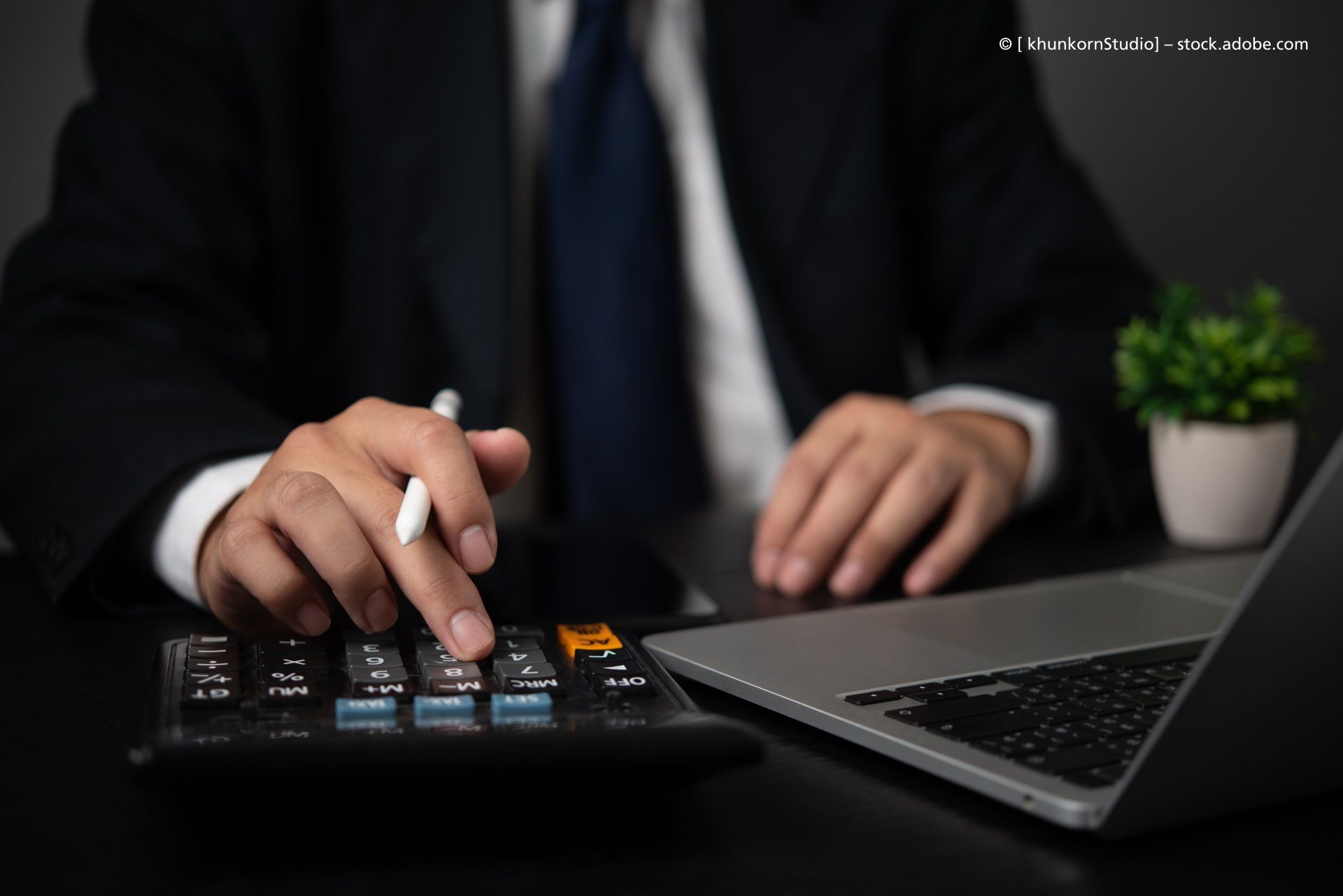 Person mit Laptop, Stift und Taschenrechner
