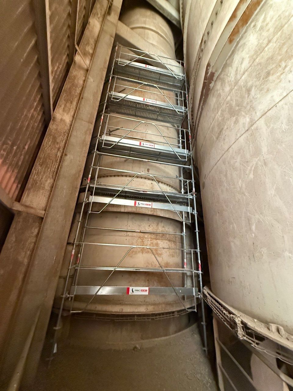 Échelle métallique abrupte à l'intérieur d'un étroit puits industriel entre des parois en béton.