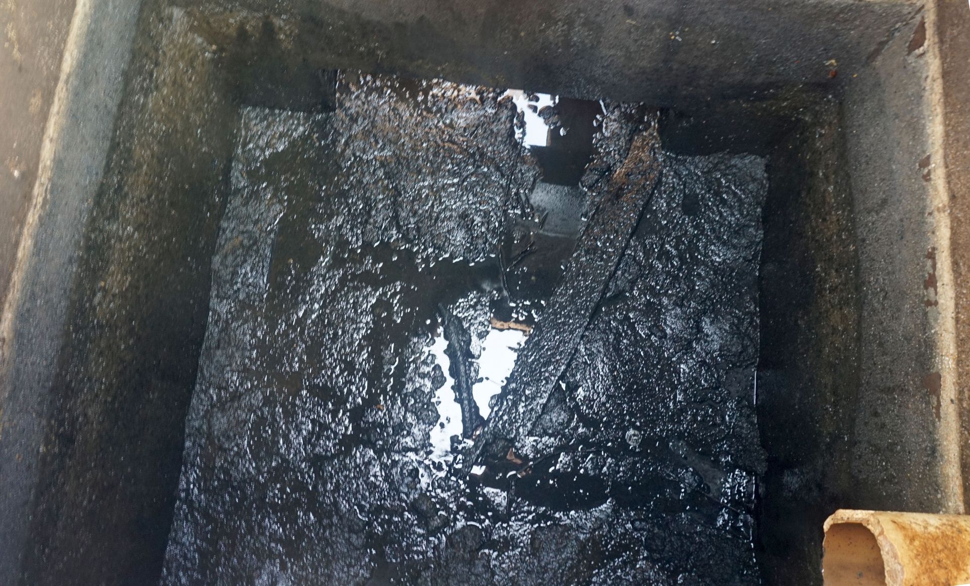 Una vista de cerca de una sustancia oscura, turbia y aceitosa en un recipiente de hormigón cuadrado.