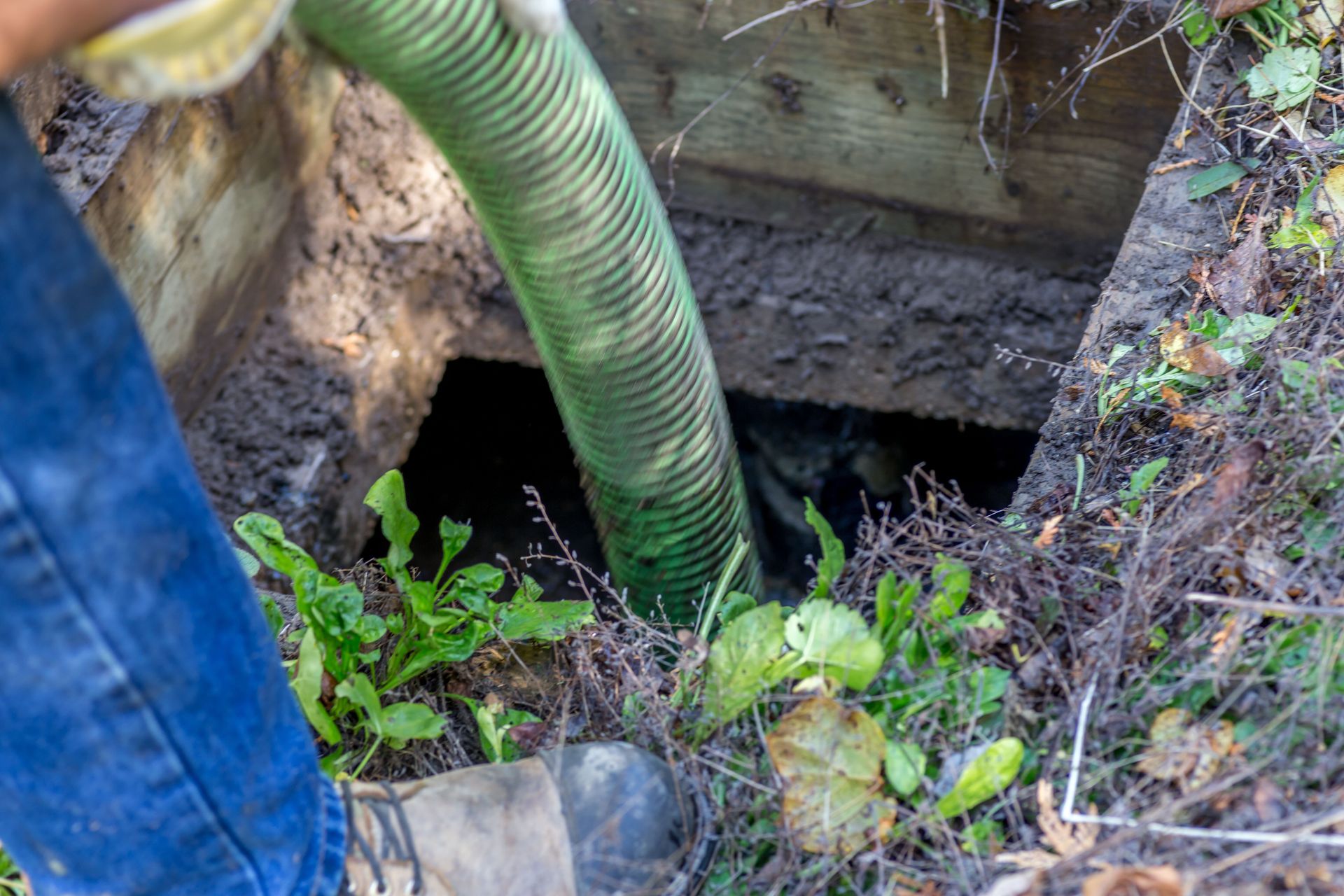 Una persona bombea agua a una fosa séptica con una manguera verde. La fosa está abierta al aire libre.