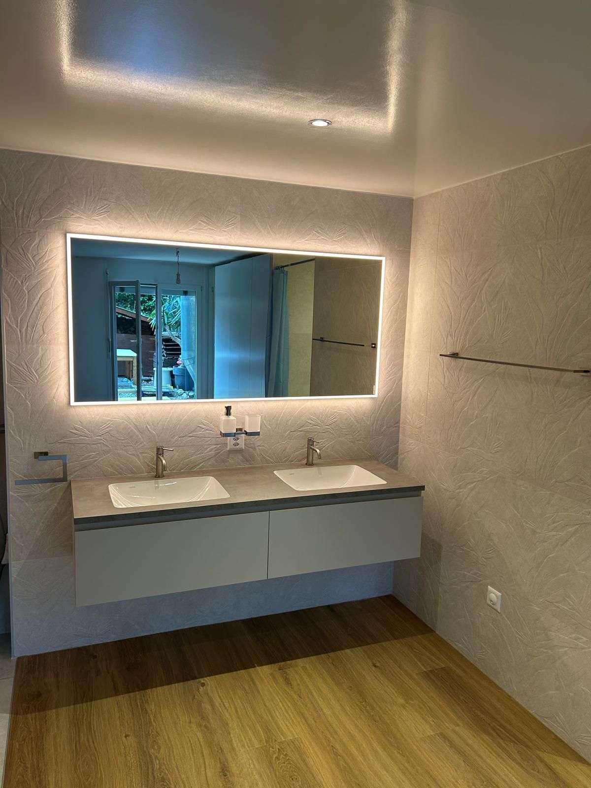 Salle de bains moderne avec meuble-lavabo à double vasque, miroir éclairé et sol imitation bois.