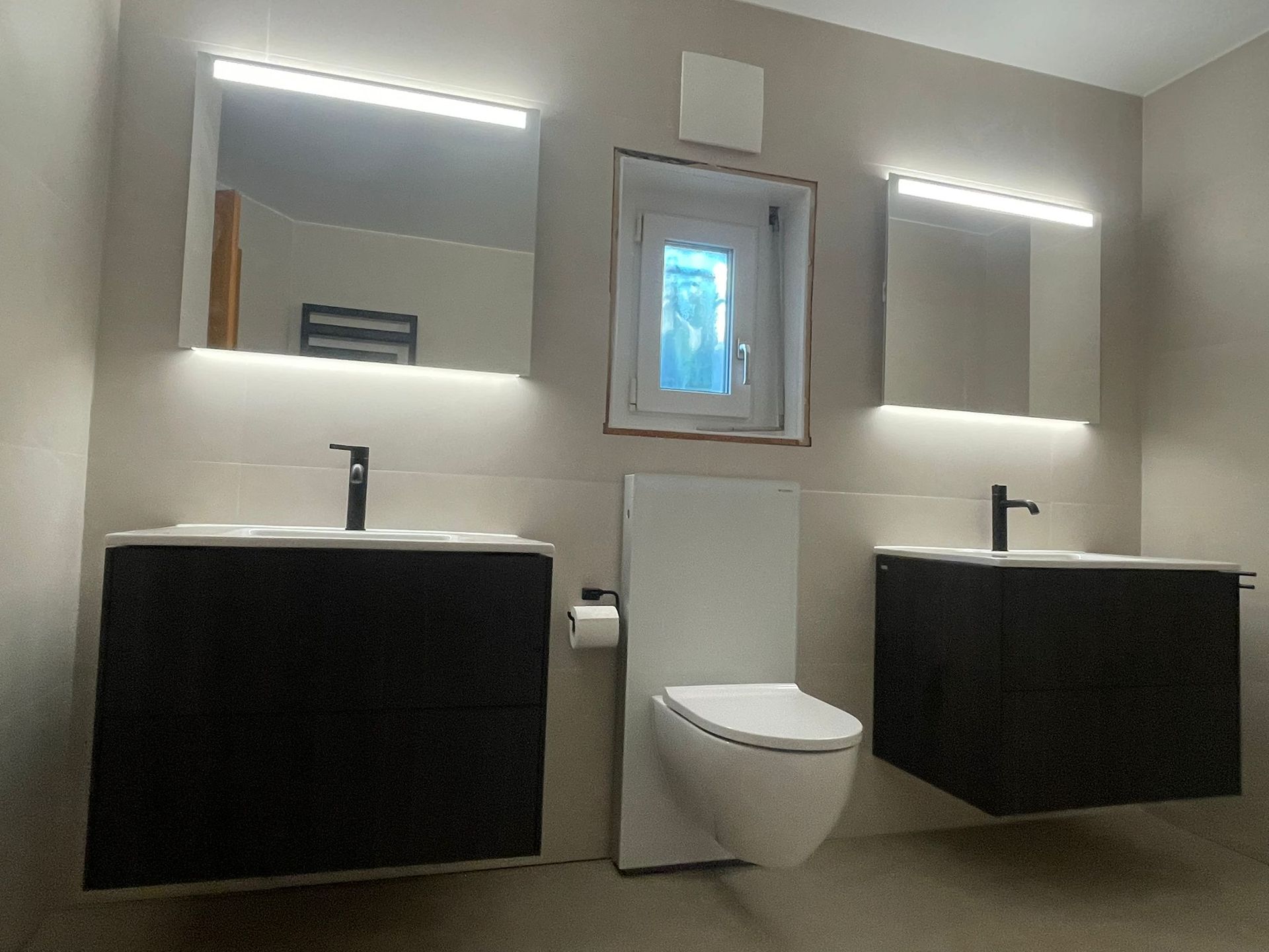 Salle de bains moderne avec deux vasques noires, des miroirs à éclairage LED et des toilettes suspendues.