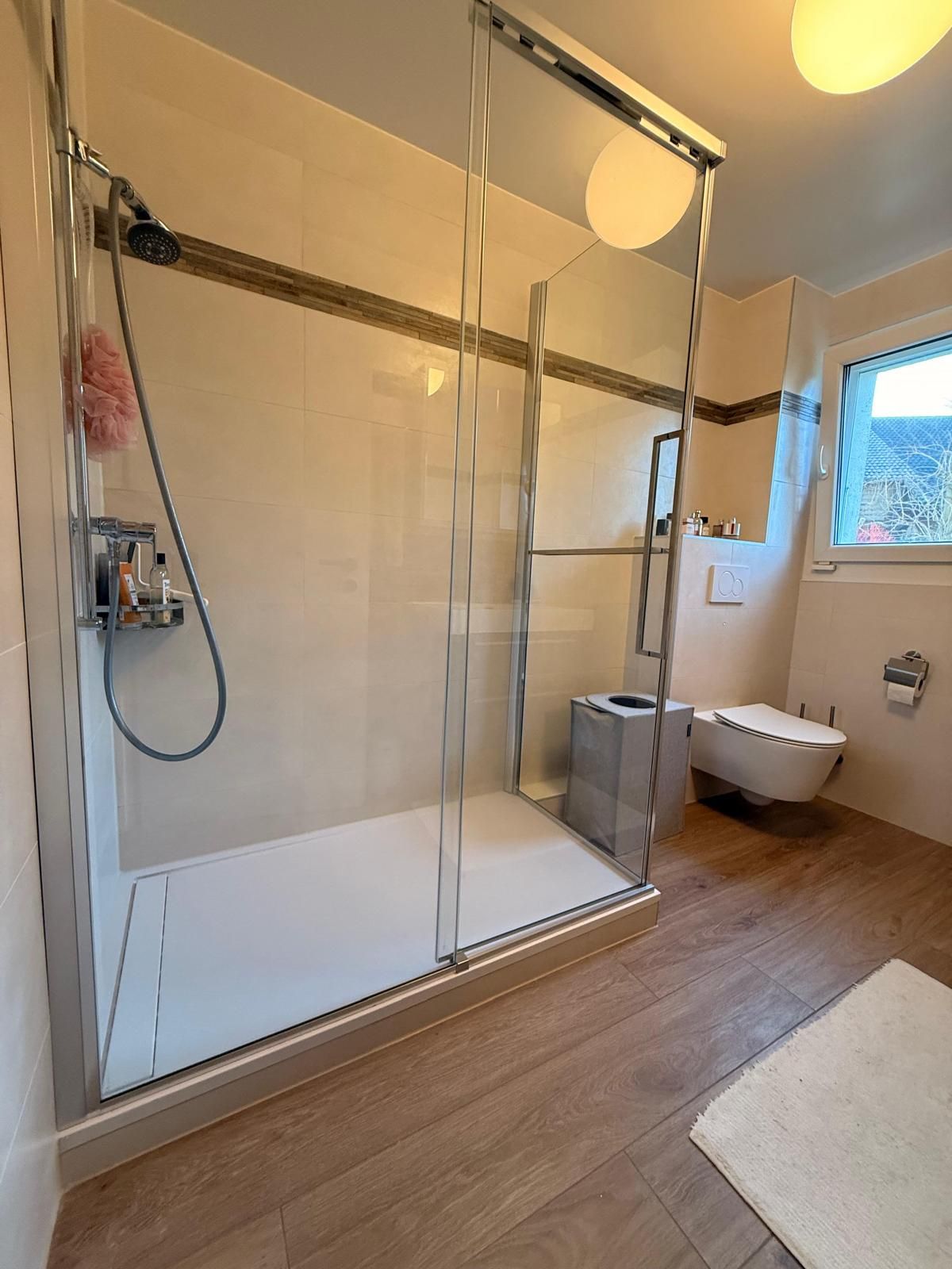 Salle de bains moderne avec douche vitrée, toilettes et sol imitation bois.