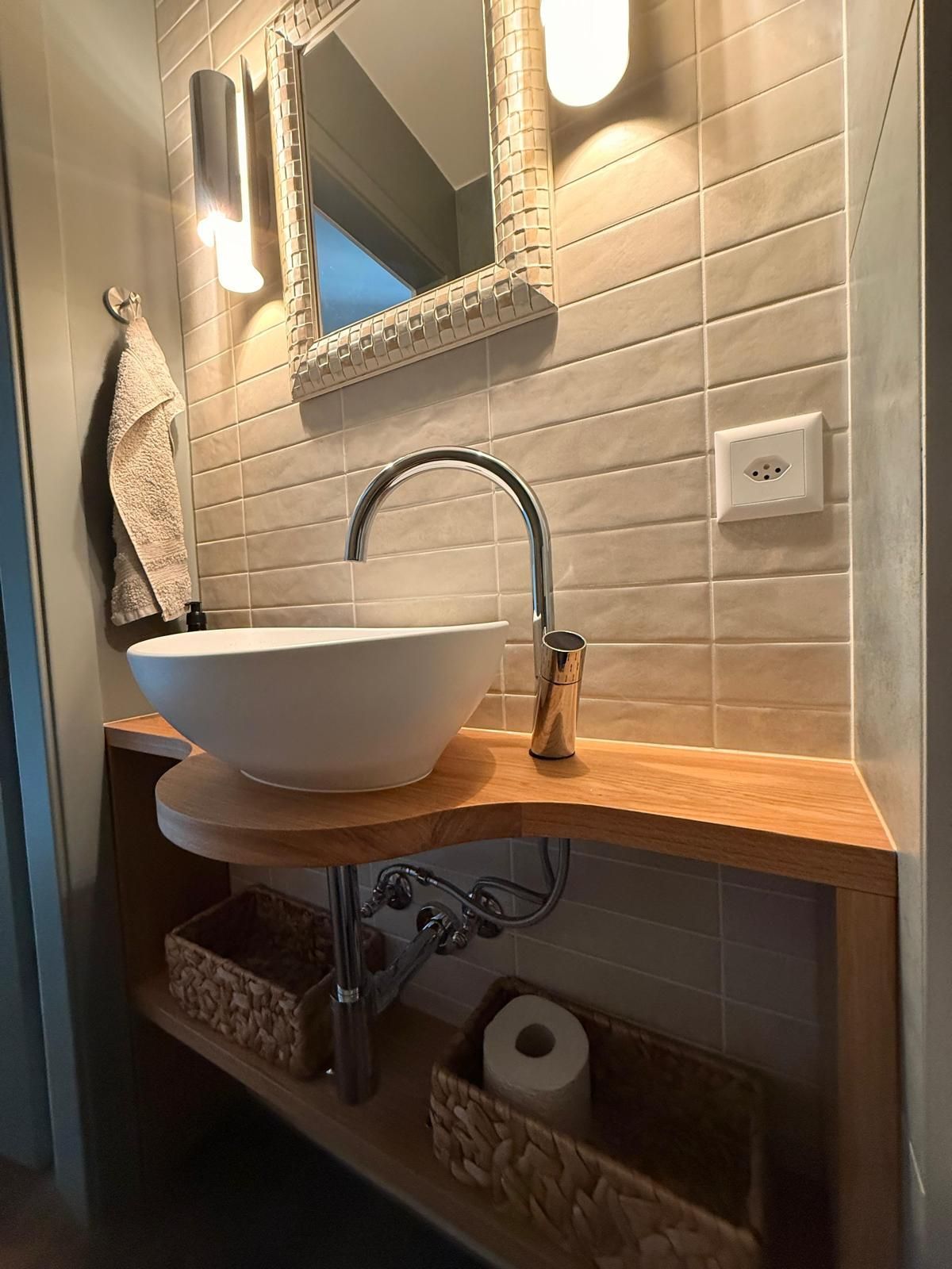 Lavabo de salle de bain avec vasque blanche, plan de travail en bois, mur carrelé et miroir.