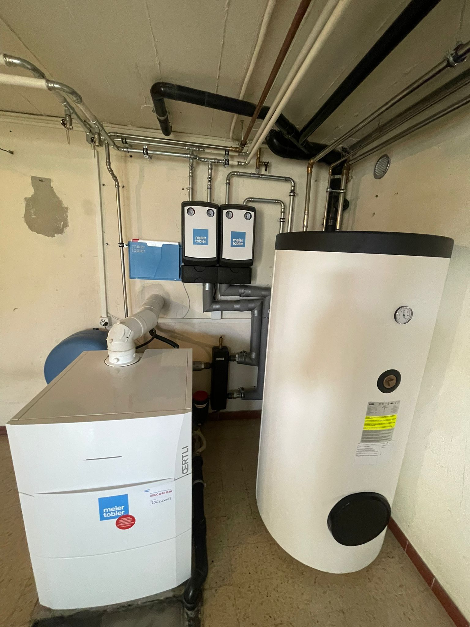 Chauffe-eau et chaudière blancs dans une buanderie avec tuyauterie et composants électriques.