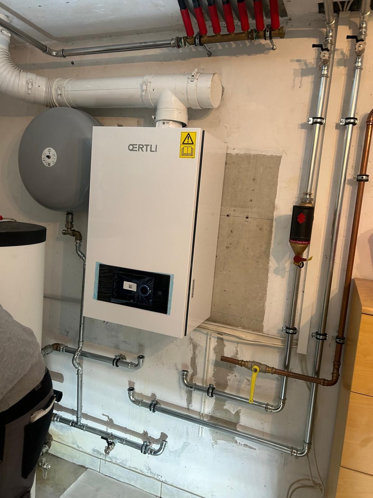 Système de chaudière blanche avec tuyaux et réservoir installé sur un mur de sous-sol.