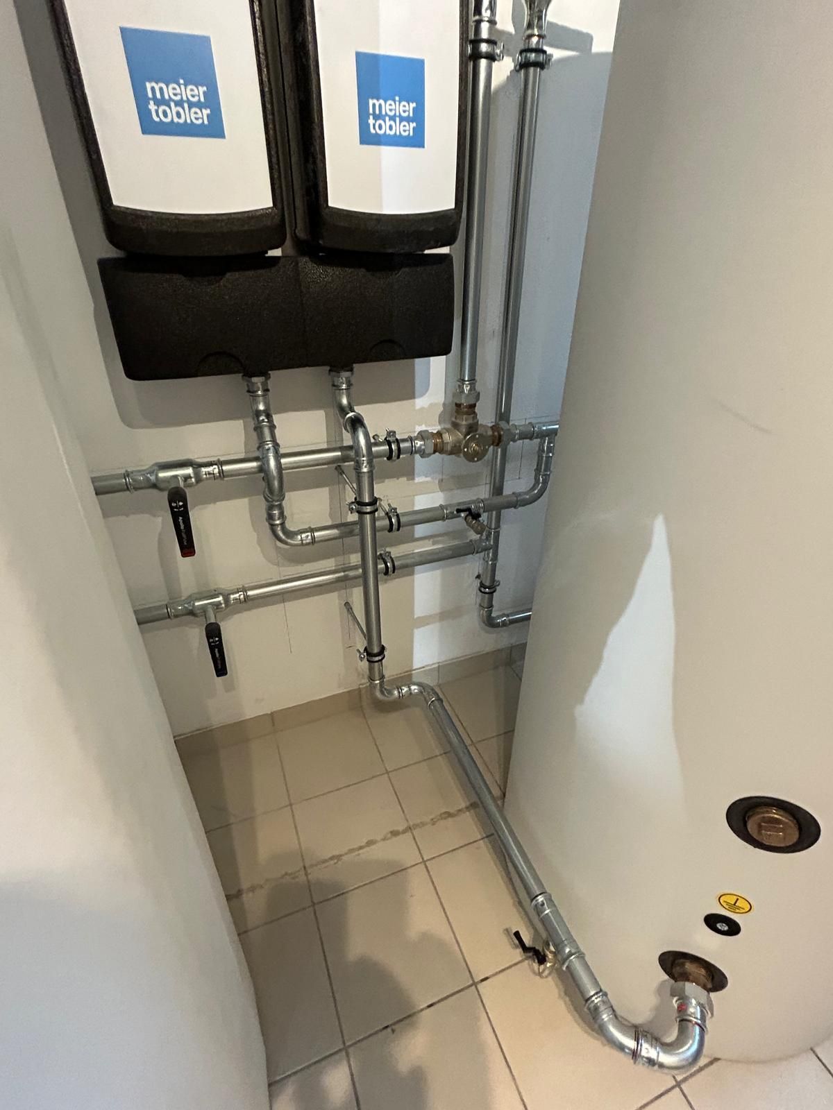 Système de plomberie avec deux chauffe-eau et tuyaux de raccordement dans une buanderie.