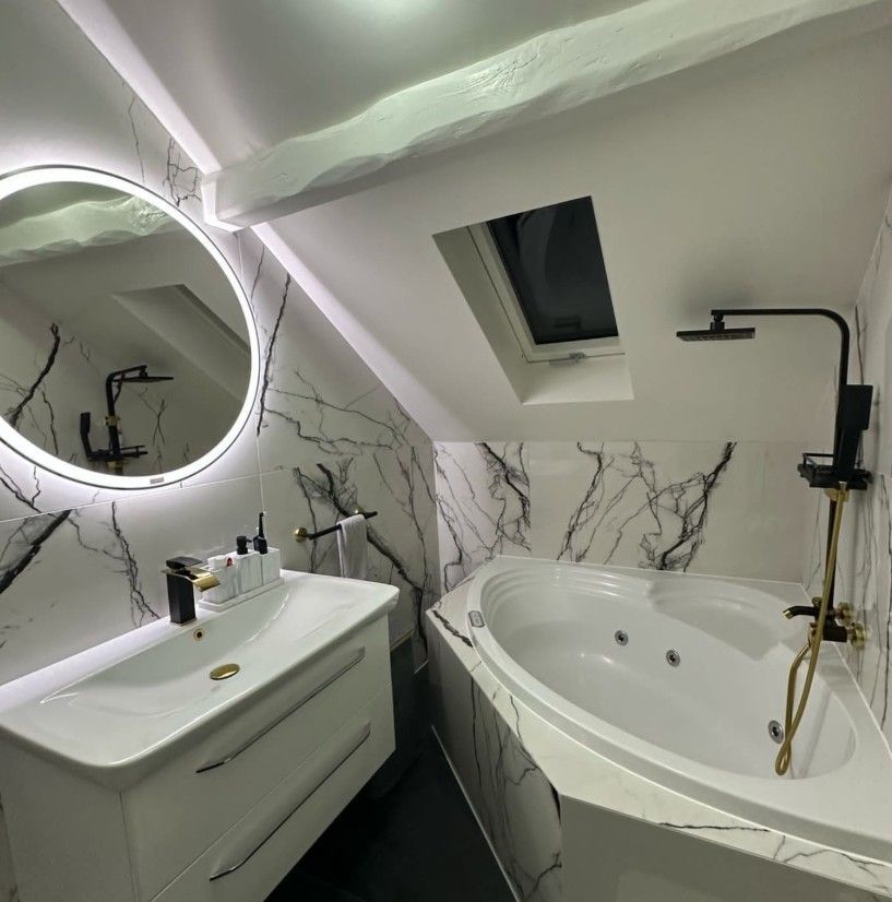 Salle de bains moderne avec carrelage blanc et marbre, baignoire ovale et robinetterie noire.