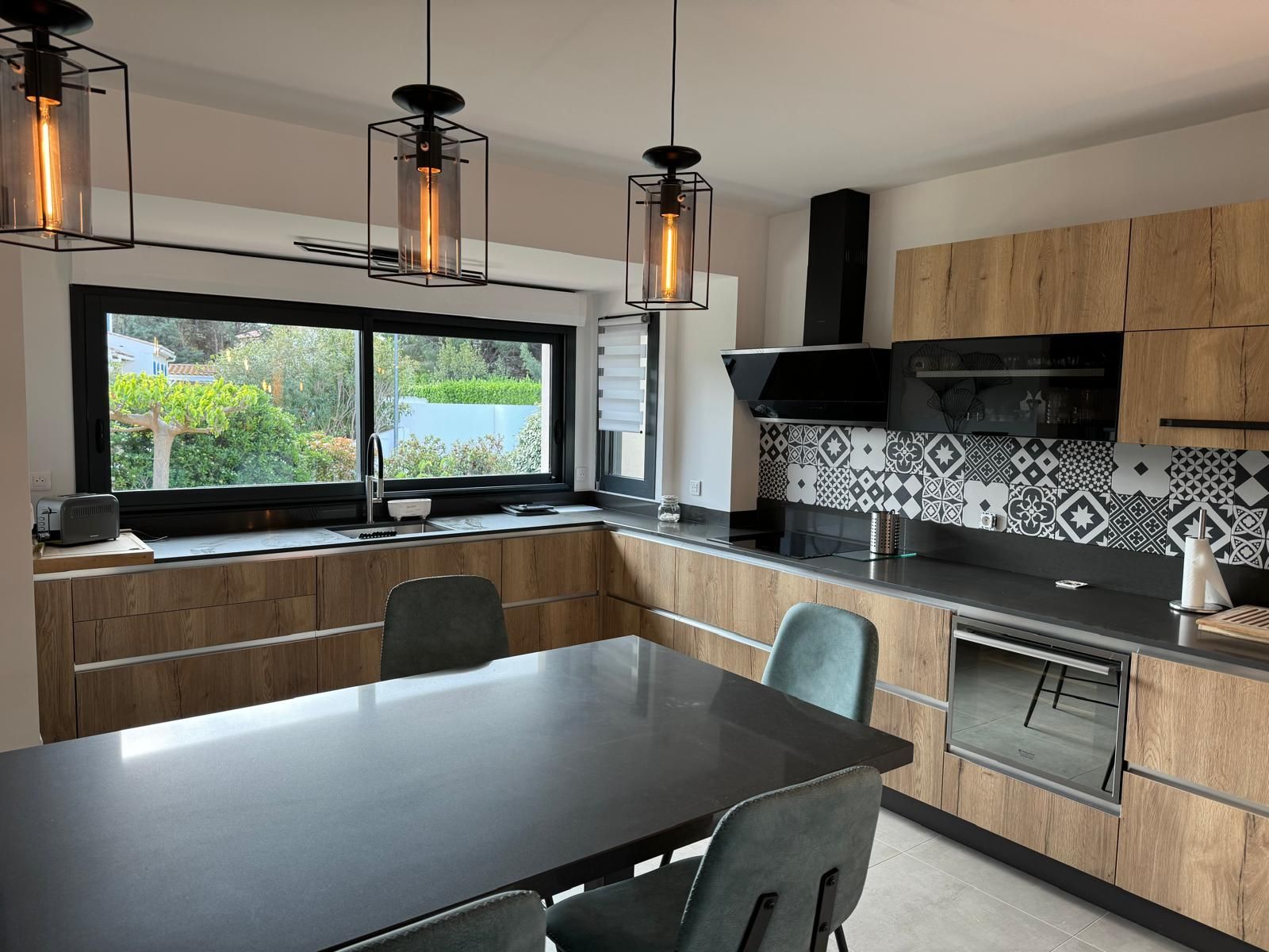 Cuisine moderne avec armoires en bois, comptoirs noirs et luminaires suspendus.