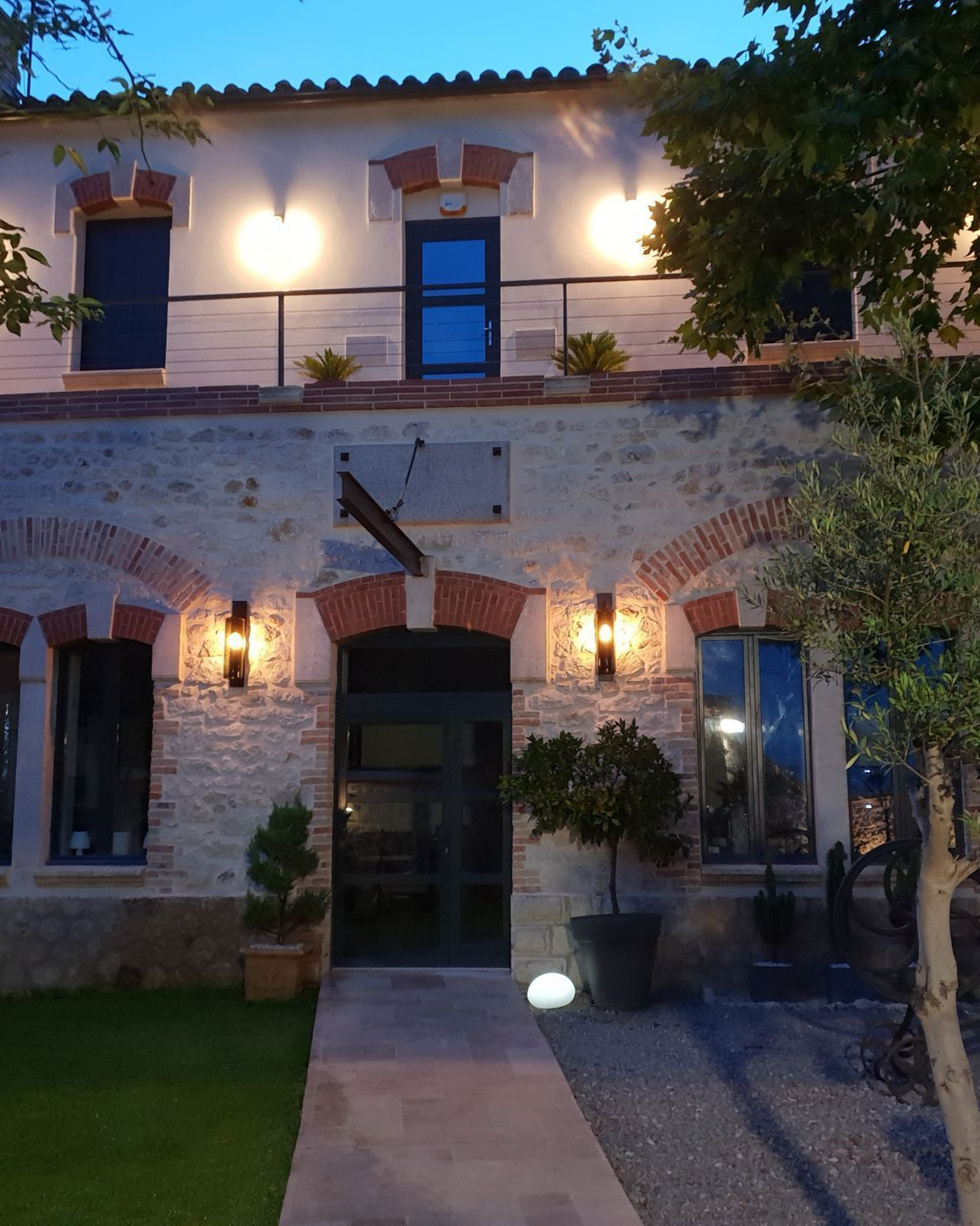 Bâtiment en pierre de deux étages avec des touches de brique, illuminé au crépuscule. Portes et fenêtres sombres.