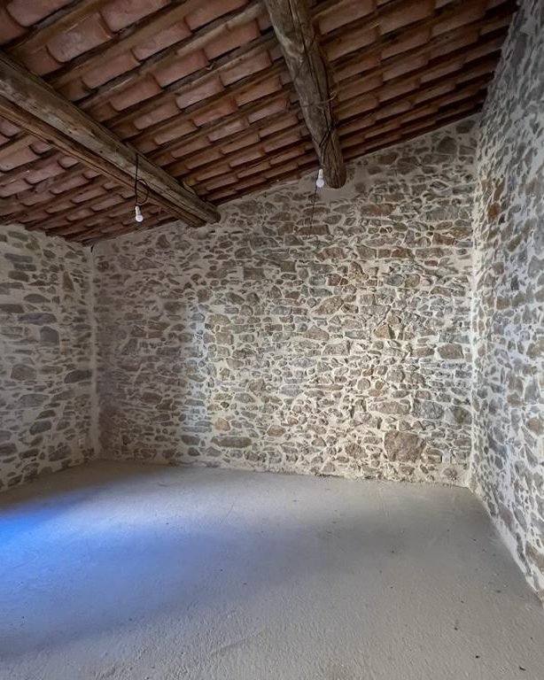 Vue intérieure d'une pièce rustique en pierre avec un toit en tuiles d'argile et un sol en béton.