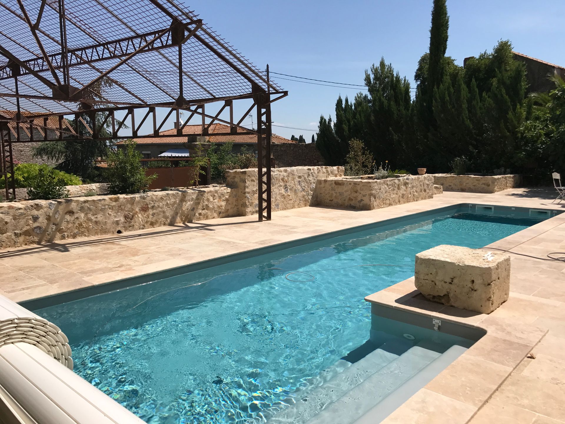 Scène au bord de la piscine avec une piscine rectangulaire, des murs en pierre et une structure en métal