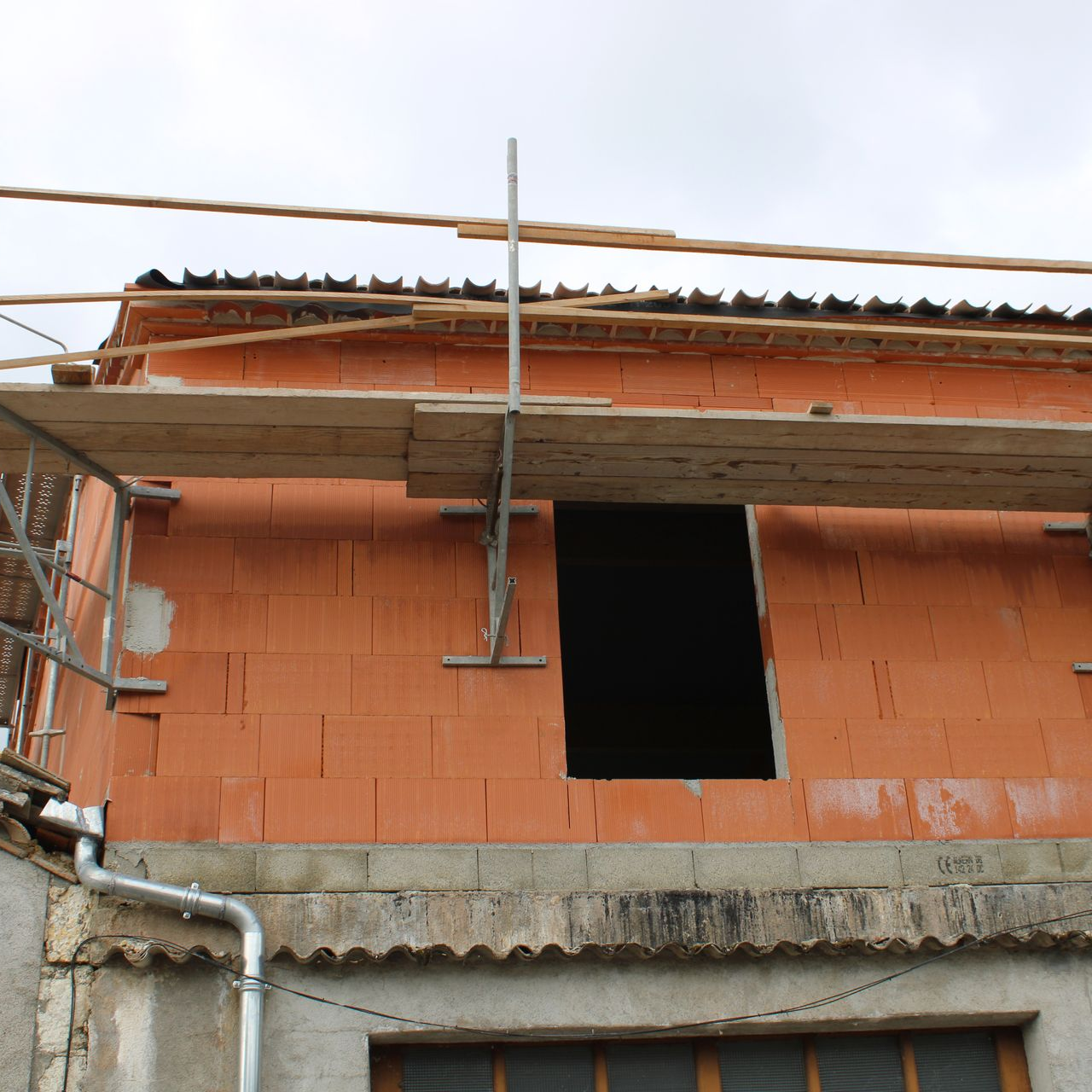 Bâtiment en construction avec une fenêtre ouverte. On aperçoit l'échafaudage et les planches du toit.