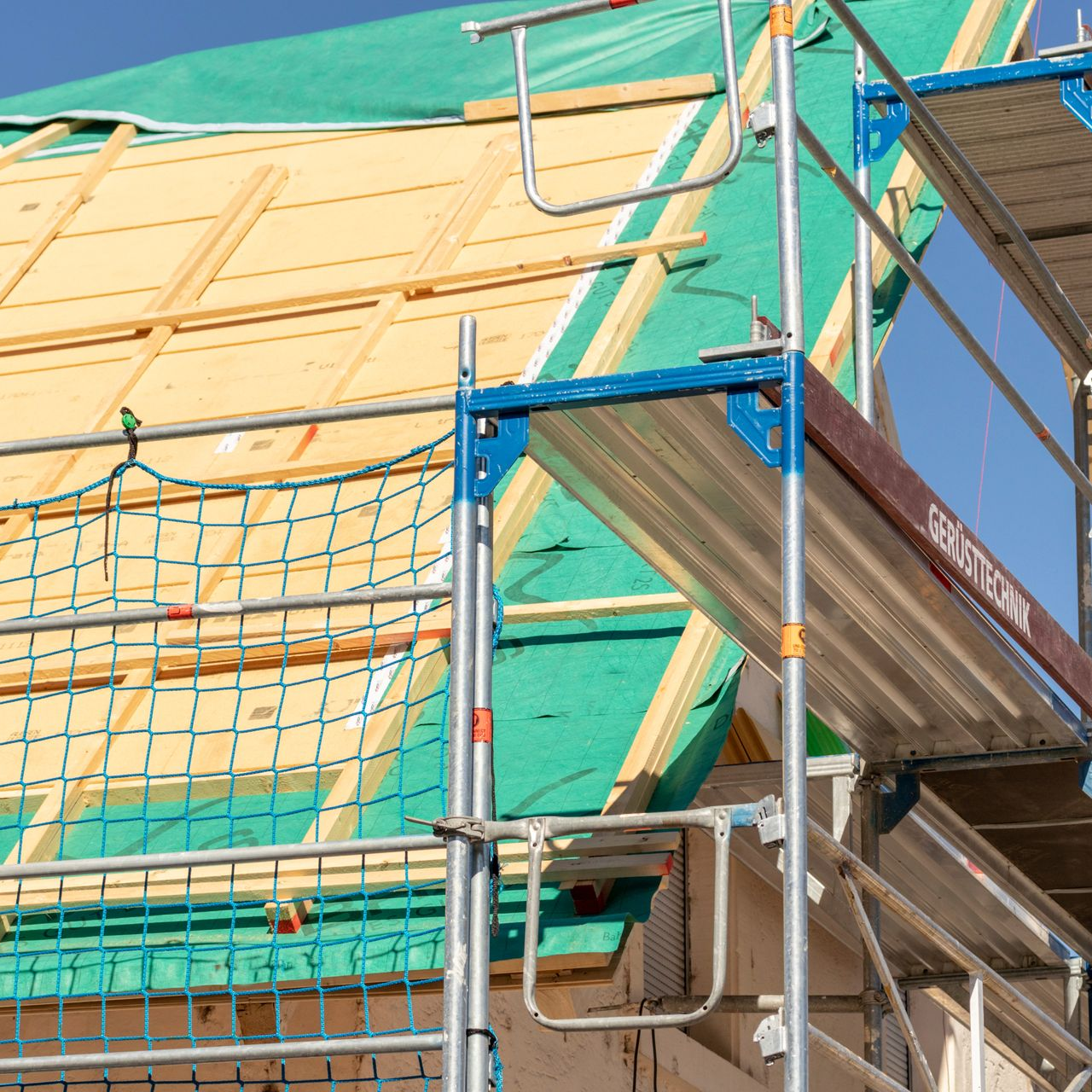 Échafaudage à côté d'un toit en construction, avec un filet de sécurité, ciel bleu.