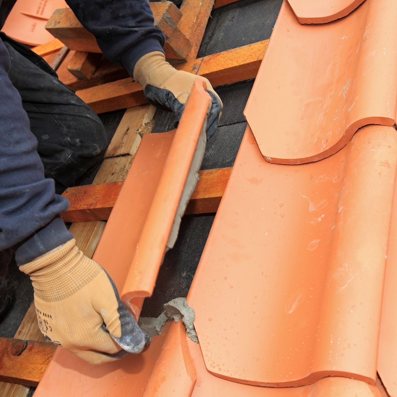 Mains d'un ouvrier installant des tuiles en terre cuite sur des lattes en bois.