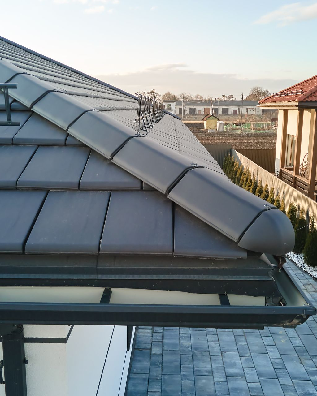 Gros plan d'un toit en tuiles grises avec gouttières, vue partielle d'une maison dans un quartier résidentiel.