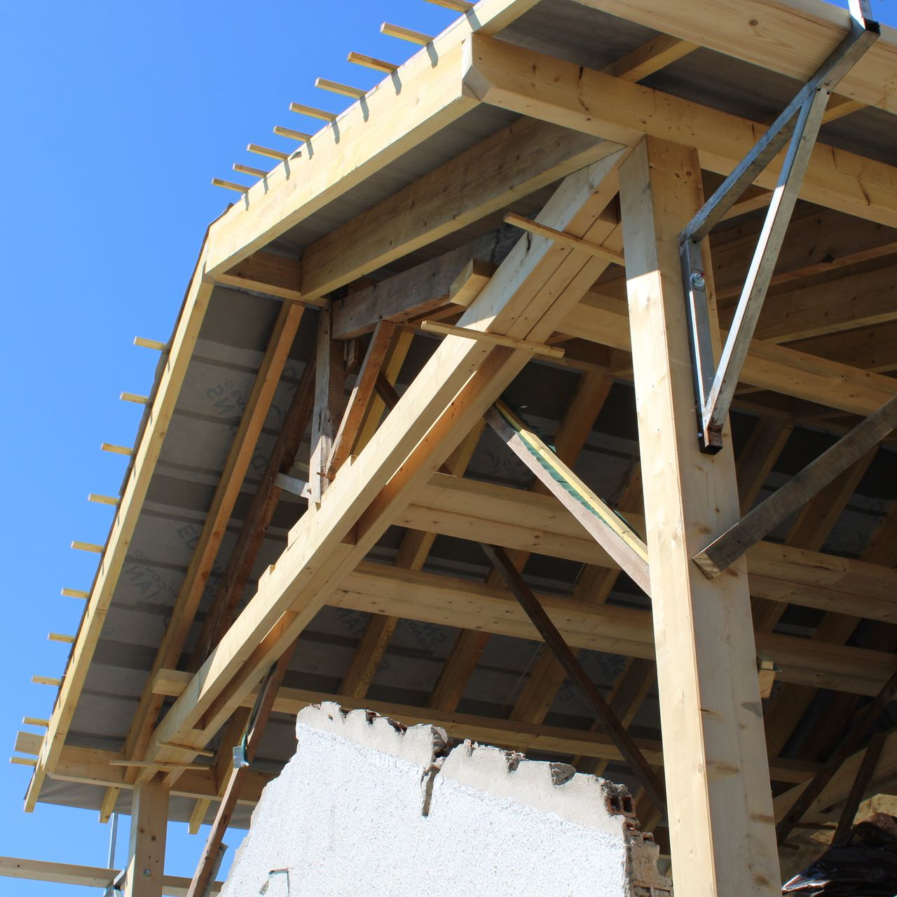 Charpente en bois d'un toit en construction contre un ciel bleu vif.