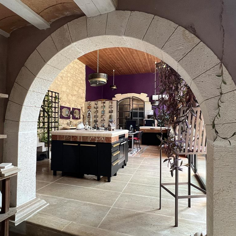 Une arche en pierre encadre une cuisine avec îlot, un mur violet et un plafond en bois.