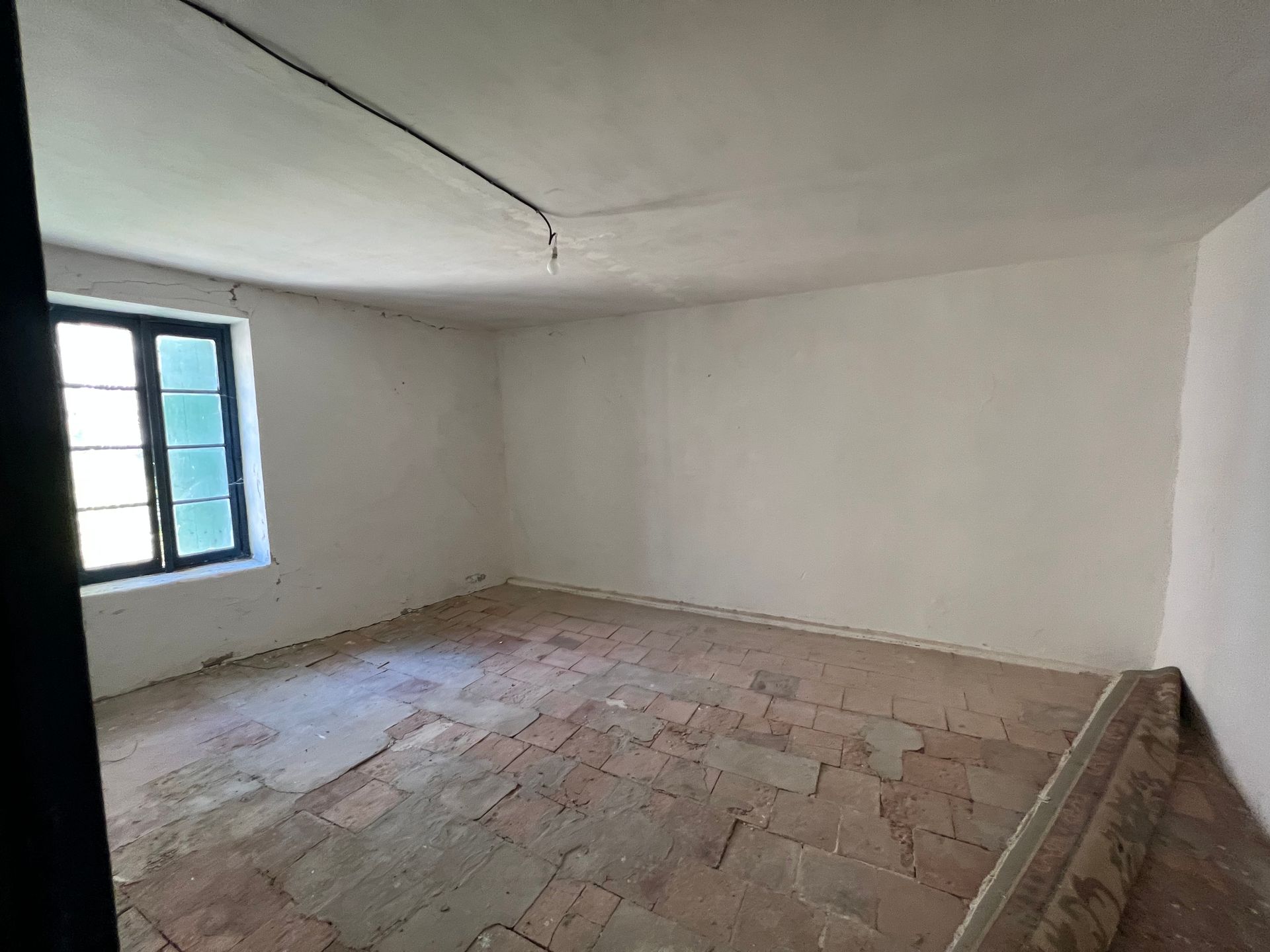 Pièce vide avec sol en briques, murs blancs, fenêtre à cadre noir.