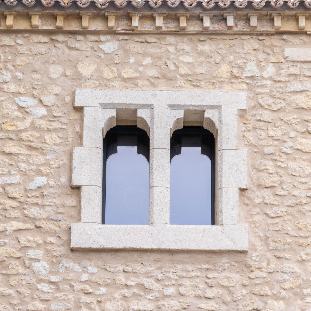 Façade en pierre avec double fenêtre encadrée en pierre claire.