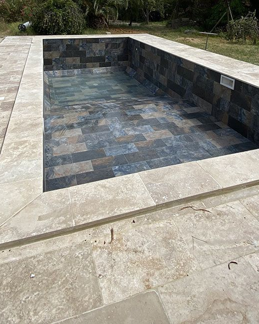 Piscine rectangulaire vide avec intérieur en carrelage foncé et contour en pierre claire.