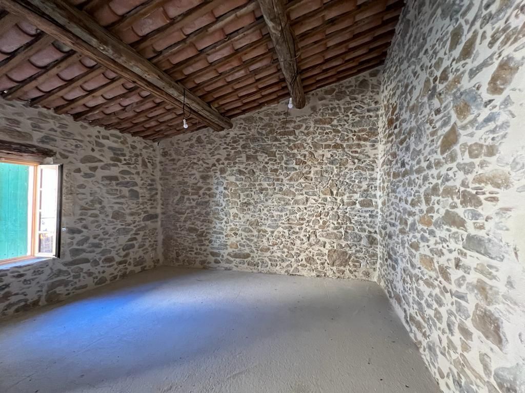 Pièce vide avec murs en pierre et plafond carrelé. Fenêtre à gauche.