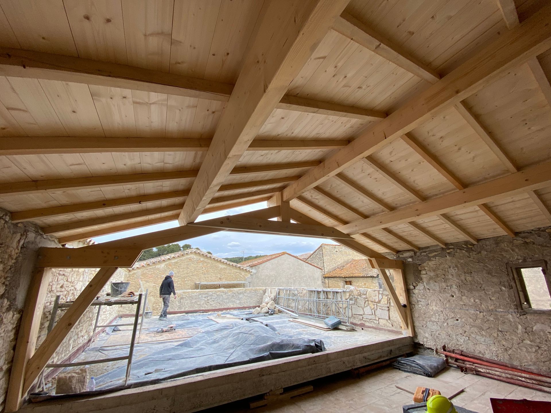 Vue intérieure d'un bâtiment en construction avec une charpente en bois et des murs en pierre.