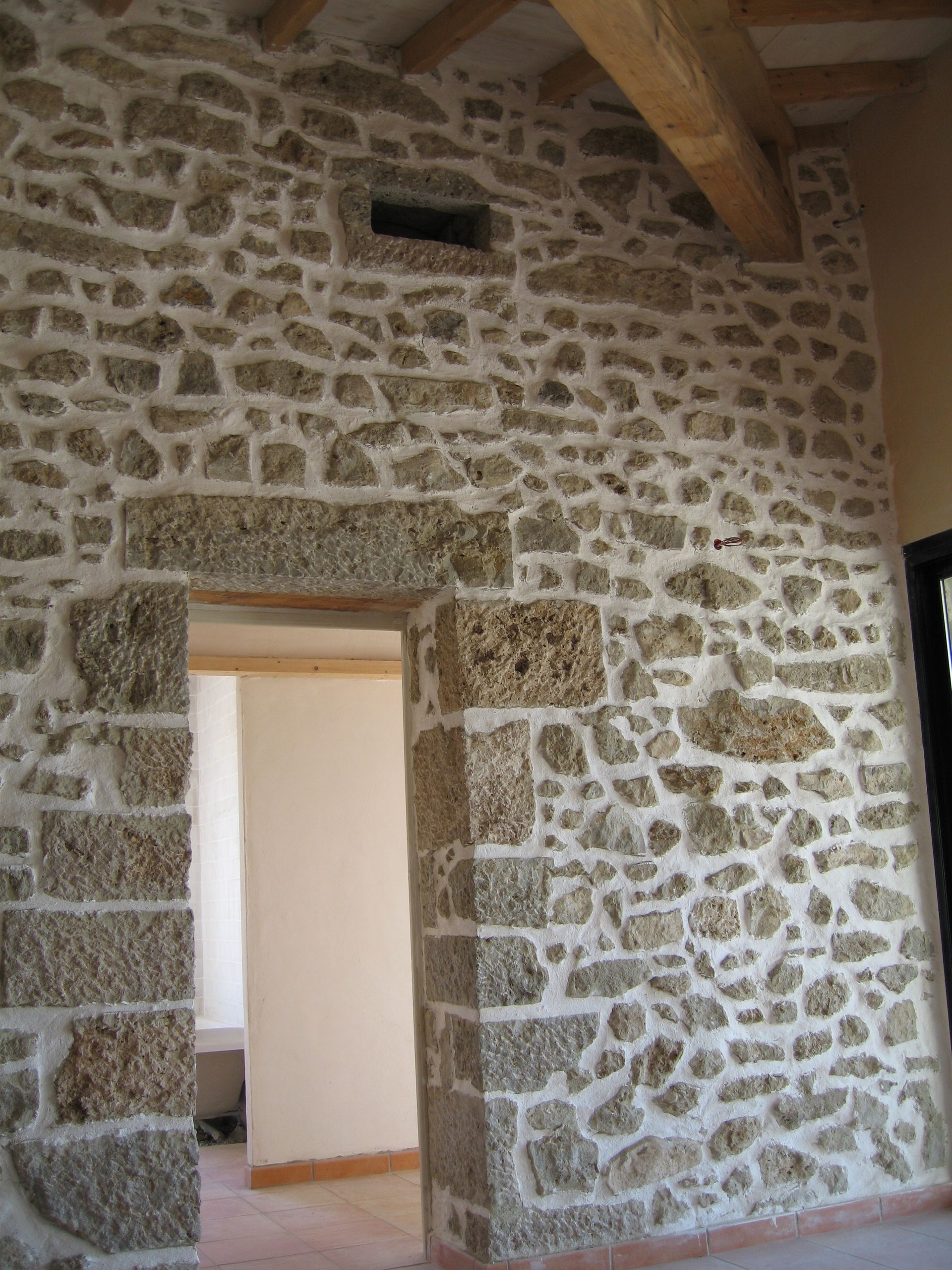 Mur intérieur en pierre avec porte et poutres en bois.