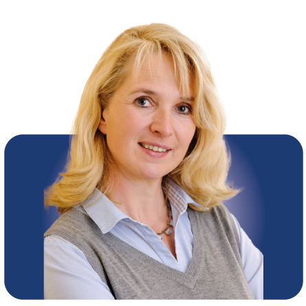 Lächelnde blonde Frau in einer grauen Weste über einem hellblauen Hemd vor blauem Hintergrund