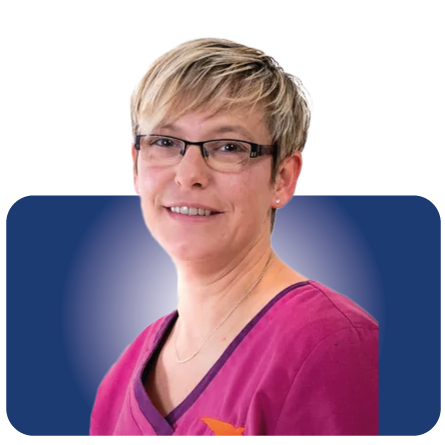 Porträt einer Person mit kurzen blonden Haaren und Brille, die ein rosa Oberteil trägt, vor blauem Hintergrund