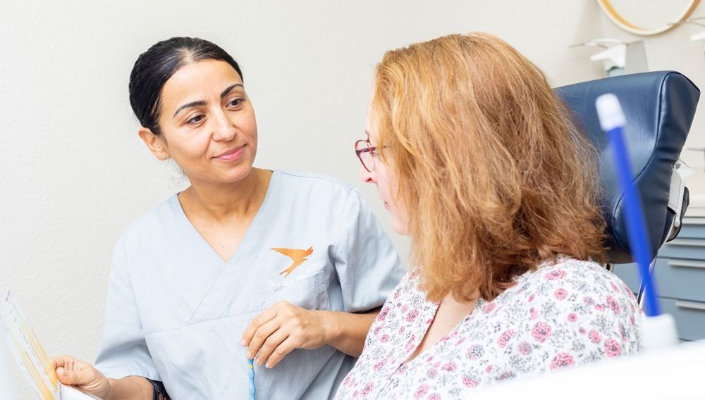 Eine Krankenschwester unterhält sich mit einem Patienten in einem Untersuchungsraum, der neben einem blauen Untersuchungsstuhl sitzt.