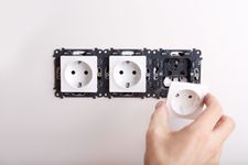 Colocación manual de un enchufe blanco en una toma de corriente de pared en un panel eléctrico parcialmente instalado.