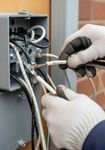 Manos enguantadas cableando una caja eléctrica abierta con cables y herramientas.