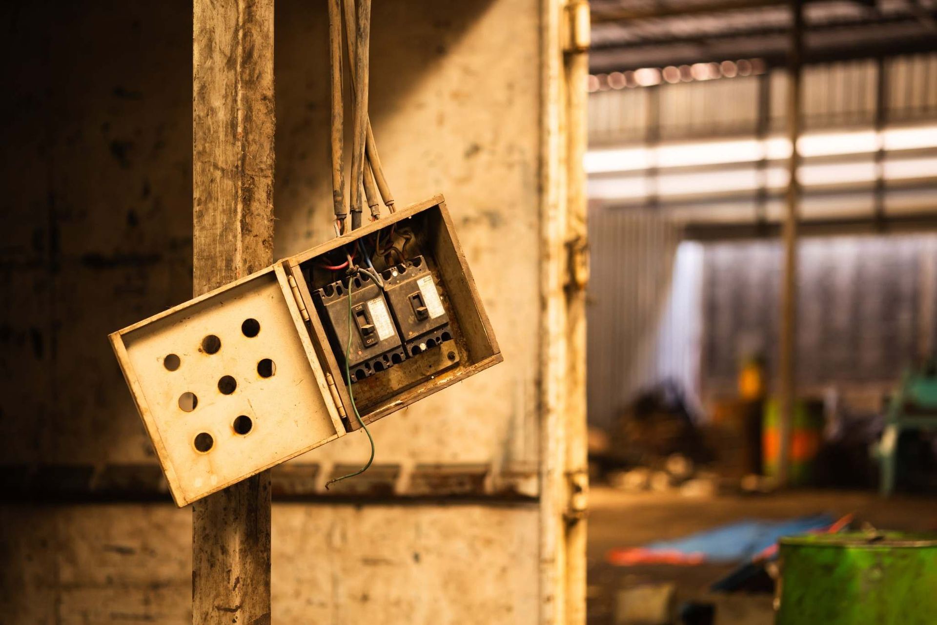 Cajas de interruptores eléctricos colgando de una pared en una habitación industrial deteriorada.