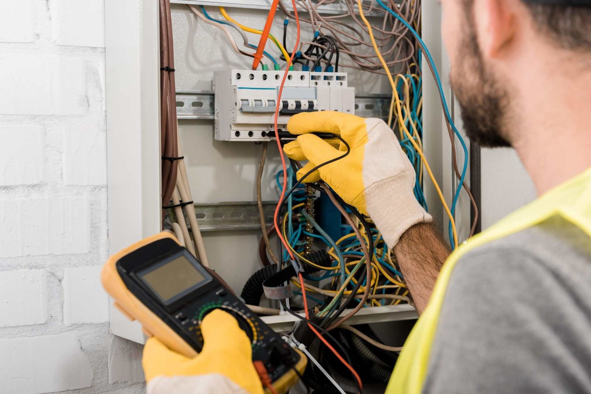 Técnico probando el cableado eléctrico expuesto en un panel de disyuntores con un medidor portátil.