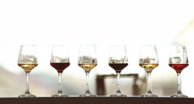 Una hilera de seis copas de vino llenas de diferentes tonalidades de vino blanco y tinto sobre un fondo brillante.