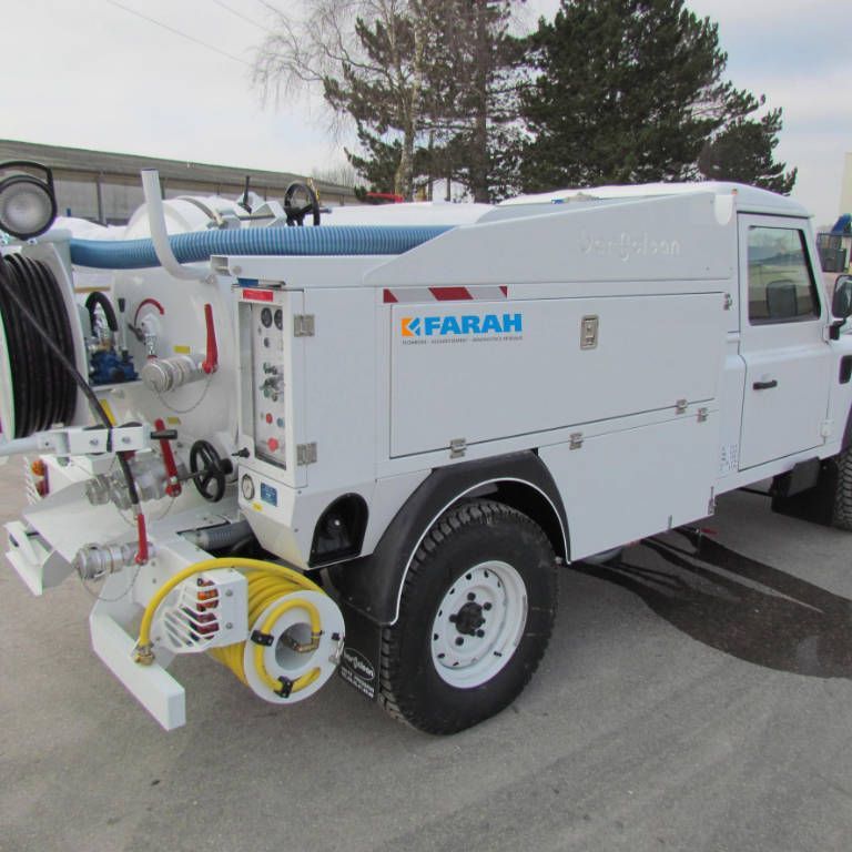 Camion-aspirateur industriel blanc avec tuyaux et réservoirs, stationné à l'extérieur sur le trottoir.