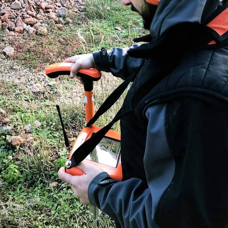 Personne utilisant un appareil de levé GPS en extérieur, sur l'herbe et les rochers.