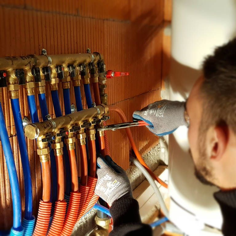 Un électricien effectue le câblage d'un panneau de commande avec des câbles bleus et orange à l'intérieur d'un coffret en bois.