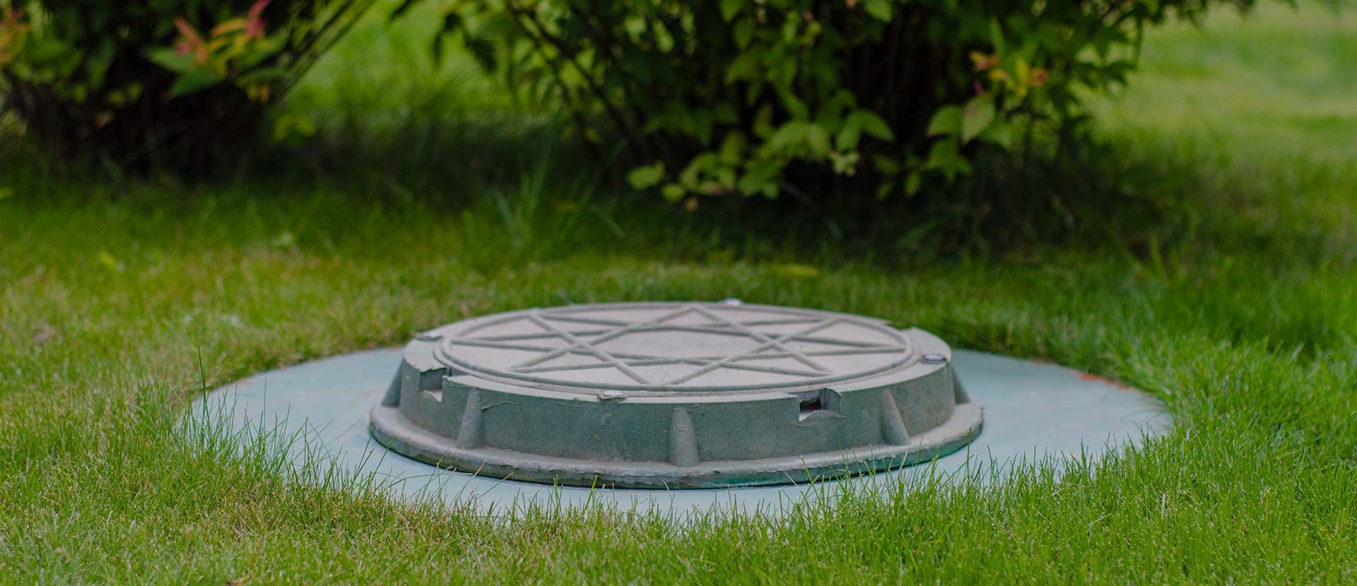 Plaque d'égout ronde en métal, entourée d'herbe verte et entourée d'un anneau de béton.
