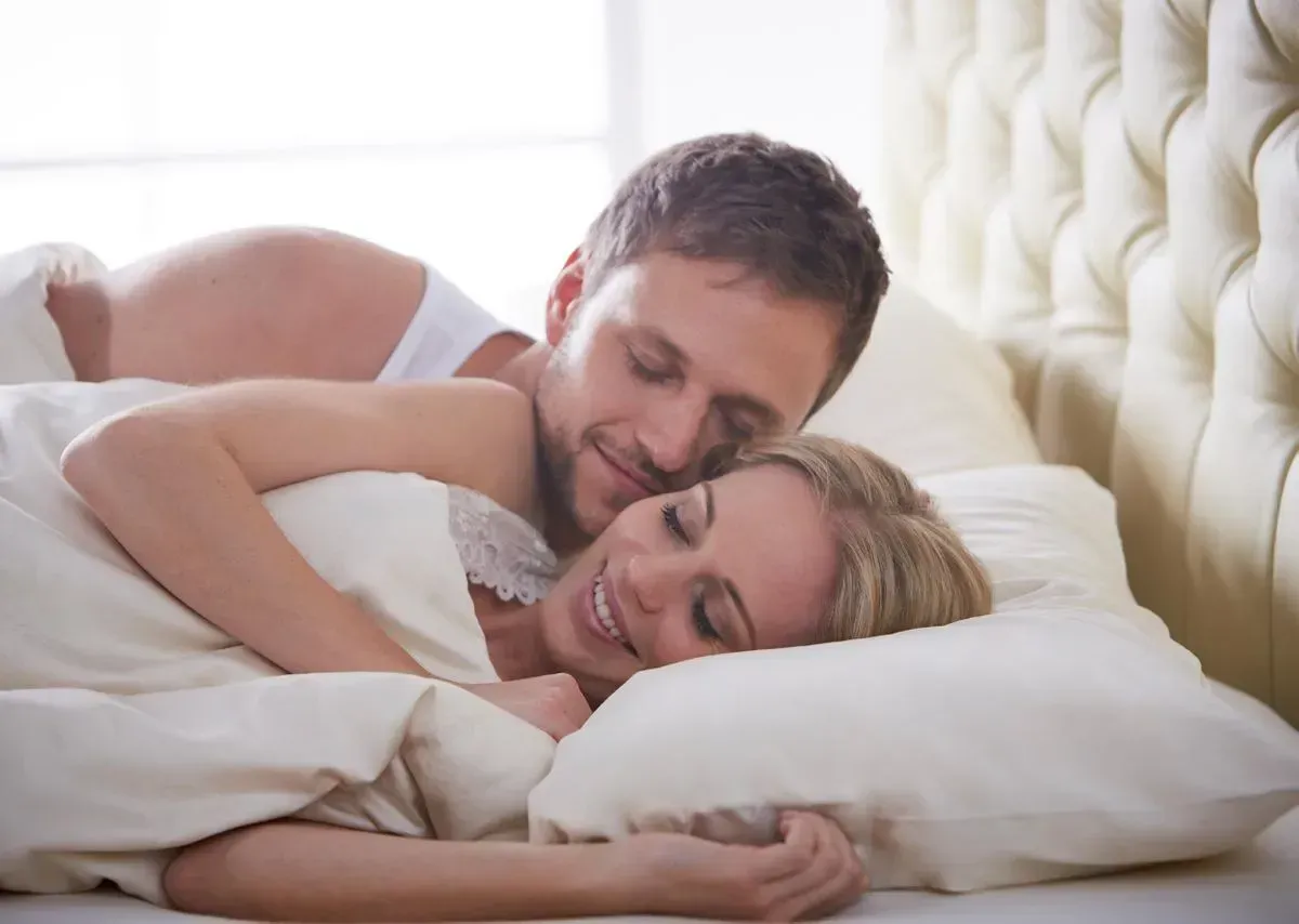 Junges Paar liegt im Bett und kuschelt mit den SAMINA Kissen und Decken