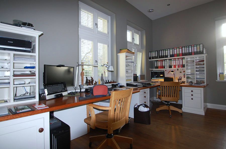 Arbeitszimmer mit langem Schreibtisch über Eck und vielen Schränken und Regalen aus weiß lackiertem Holz