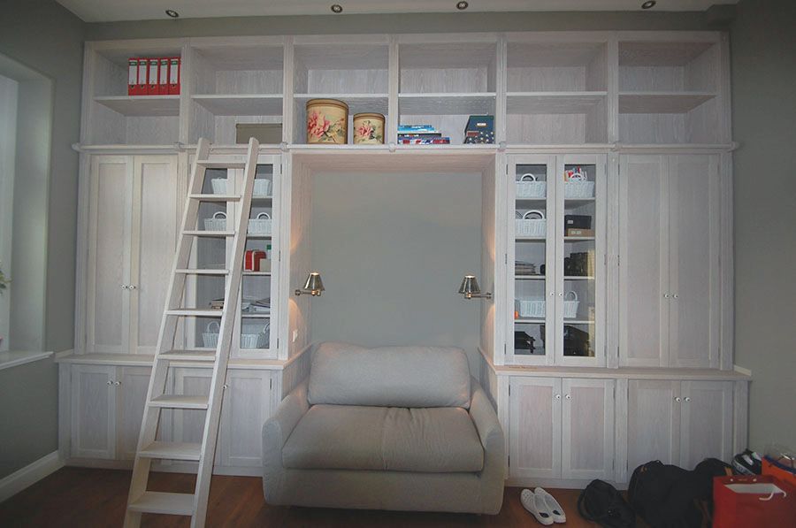 Einbauschrank mit Regalen und verschiebbarer Leiter. In der Mitte des Schrankes mit Aussparung für einen Sessel mit Lampen
