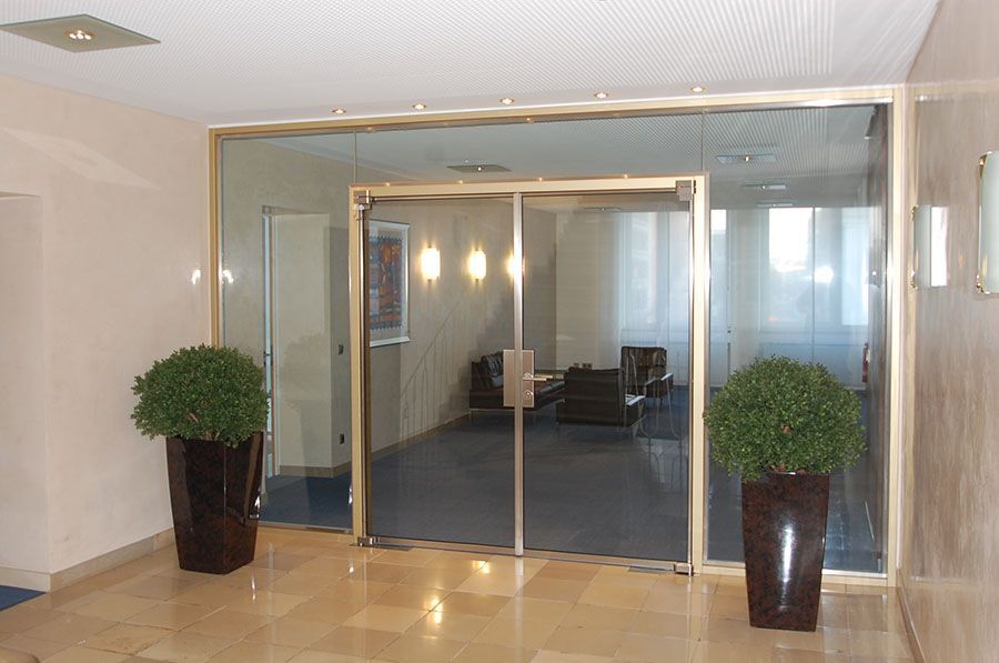 Eingangstür aus Glas und Metallrahmen mit Glasumrandung als Wand