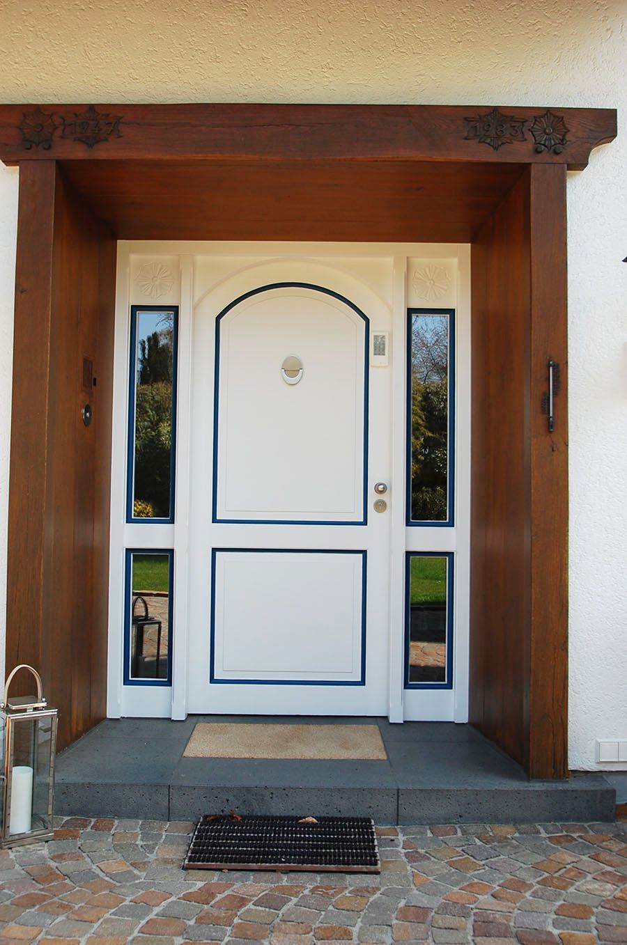 Haustüre aus weißem Kunststoff mit blauer Verzierung und Fenstern links und rechts von der Türe
