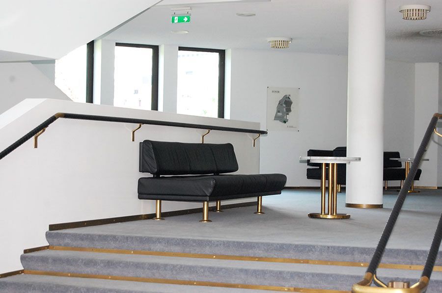 Gepolsterte Bank mit Lehne und einem kleinen runden Tisch an einer Treppe in einem Bürokomplex