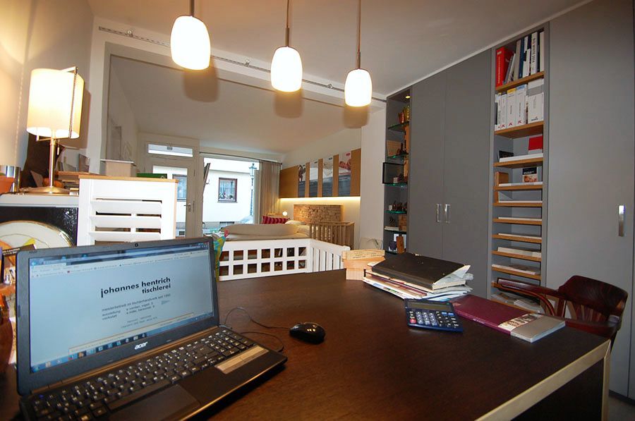 Rechts im Hintergrund ist ein Einbauschrank und im Vordergrund steht ein Tisch mit einem Laptop und Büromaterial darauf